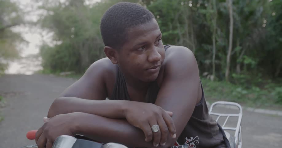 A young man leans forward on his motorcycle in the street