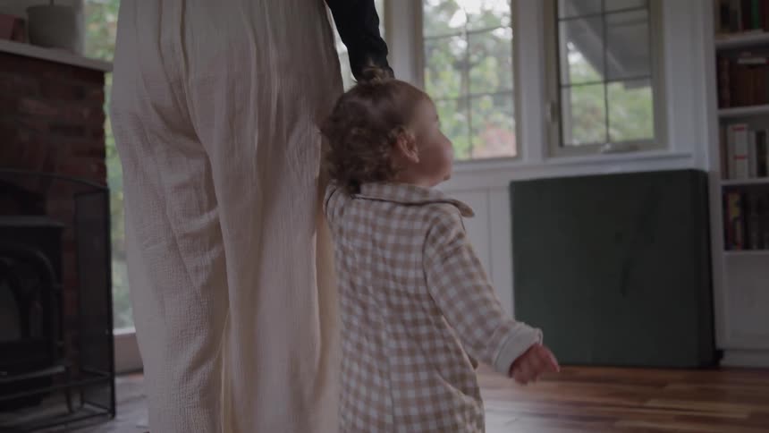 A parent holds their toddlers hand helping them walk across a room highlighting the small but significant steps of a childs early development