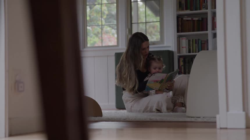 A mother reads a book for her child on the floor at home
