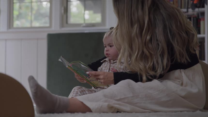Woman sitting on the floor reading a book with a small child