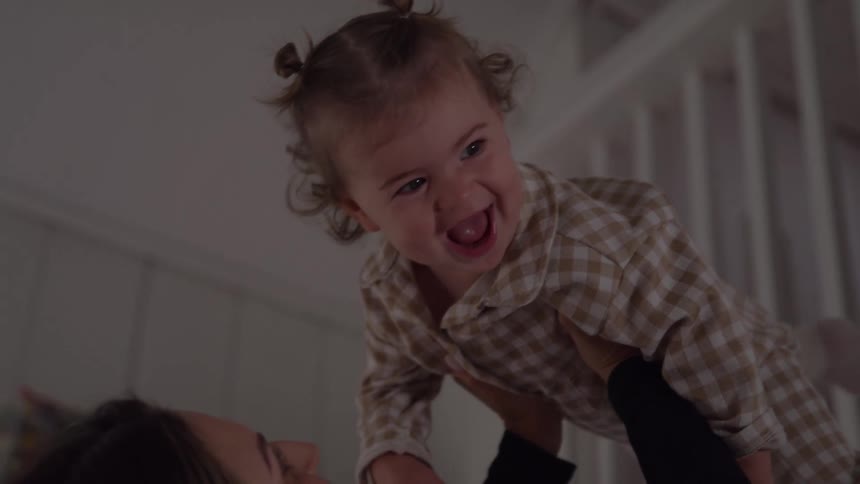 Smiling child in plaid shirt being lifted by mother indoors