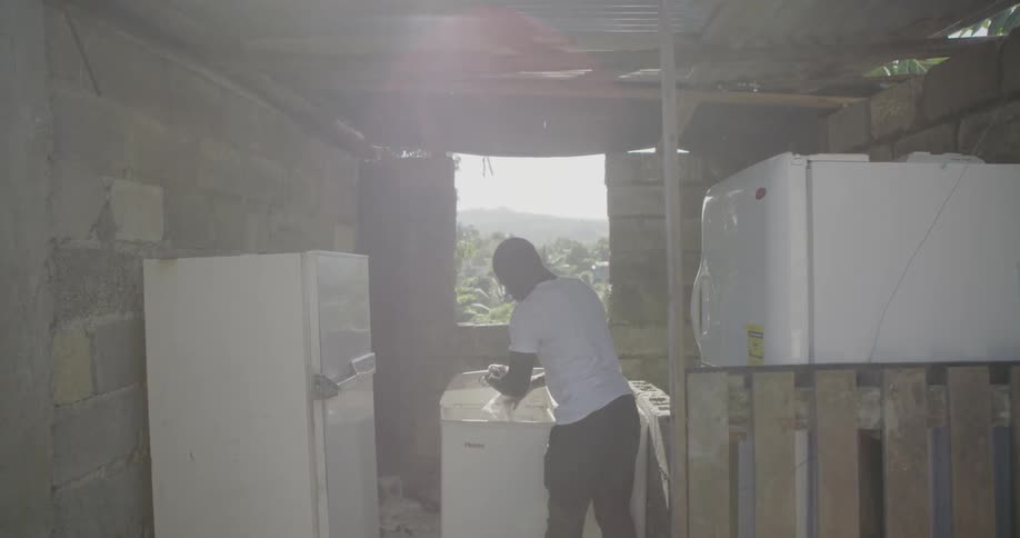 A man is washing his shirt in a utility shack