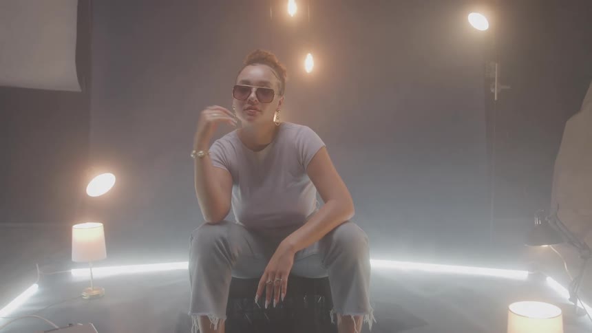Woman wearing sunglasses and an outfit that includes unhemmed pants poses on a set lit by several lamps