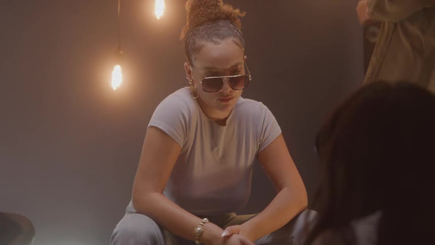 Woman wearing sunglasses and a light tshirt sitting in a room lit by hanging bulbs