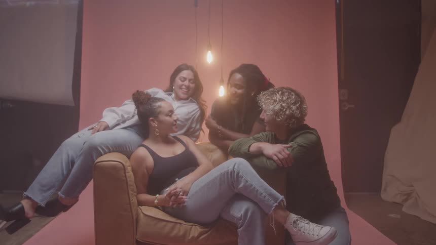 Four friends pose smiling in a studio with a pink backdrop and hanging light