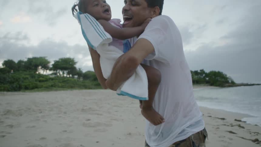 A man is standing on a beaching holding and kissing his daughter