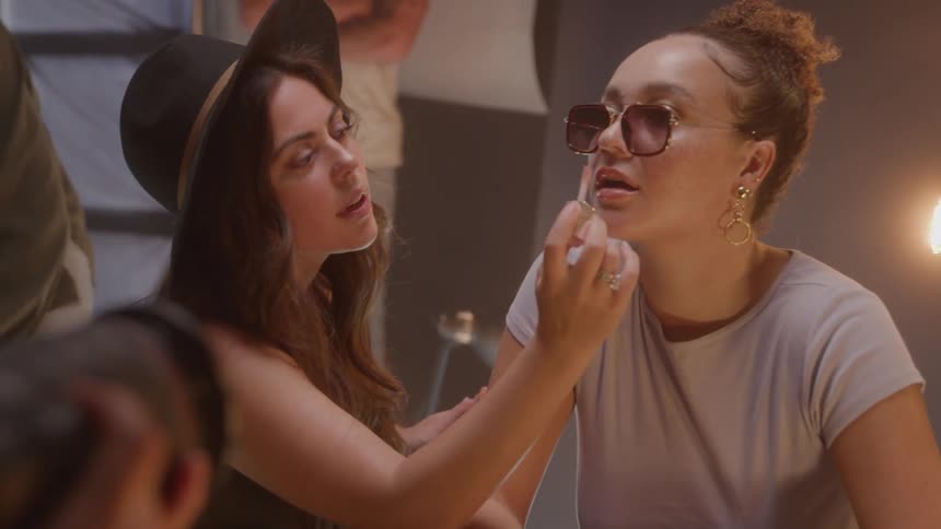 Makeup artist applies lipstick to model wearing sunglasses during photoshoot