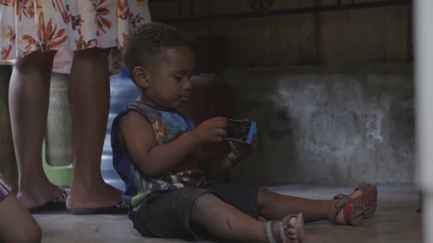 A child plays with a truck near a woman's feet