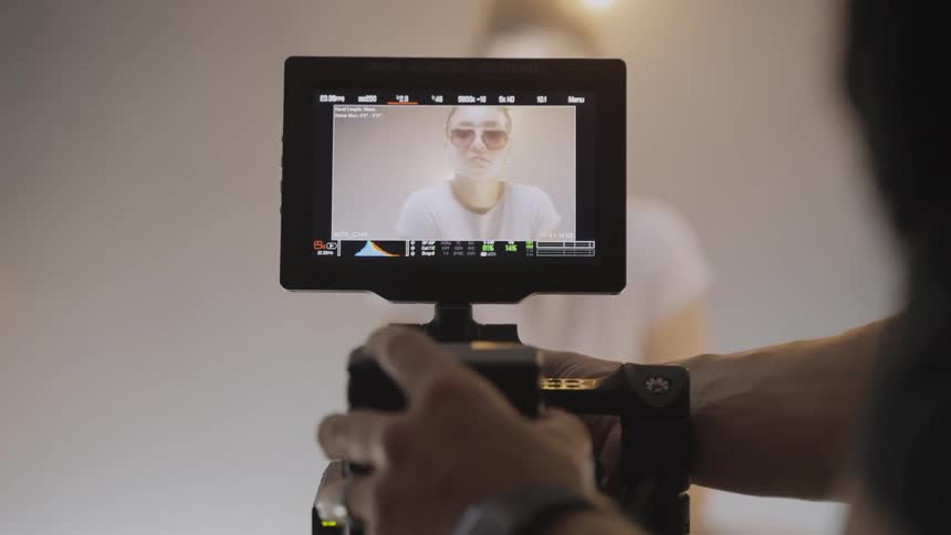 A video camera is filming a person with the live view screen showing the subject the person on the screen is wearing sunglasses and a white tshirt