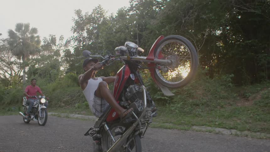 Motorcyclists pop wheelies outside on a sunny day