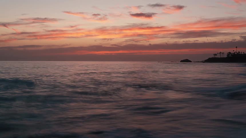Gentle waves meet the shore under the orange sunset sky