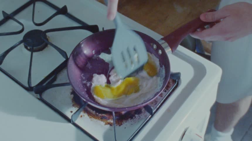 A person fries eggs in a small pan on a gas stove