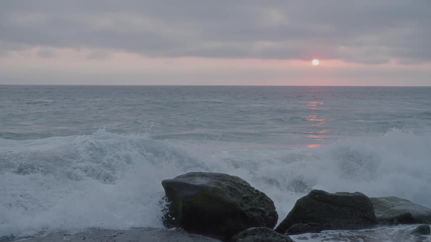 Strong waves crashing against rocks during a cloudy sunset