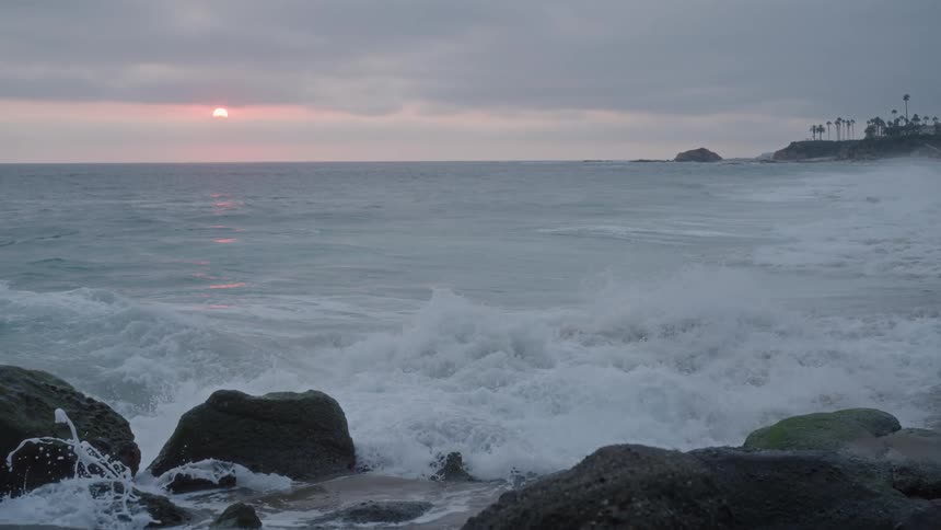 Waves crashing against rocks on the beach during a cloudy sunset