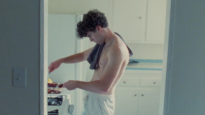 A shirtless man is cooking in a kitchen