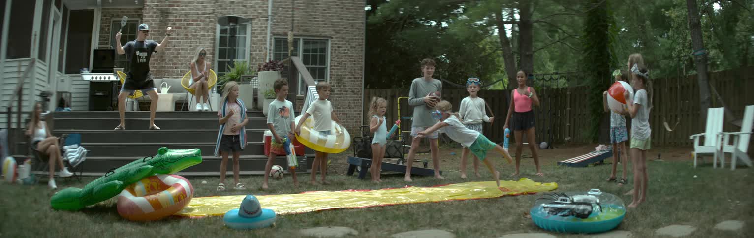 Children play on a water slide in the backyard while adults watch