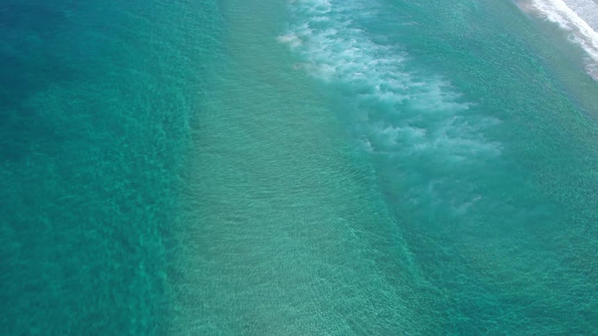 Gentle waves breaking over the turquoise sea seen from above