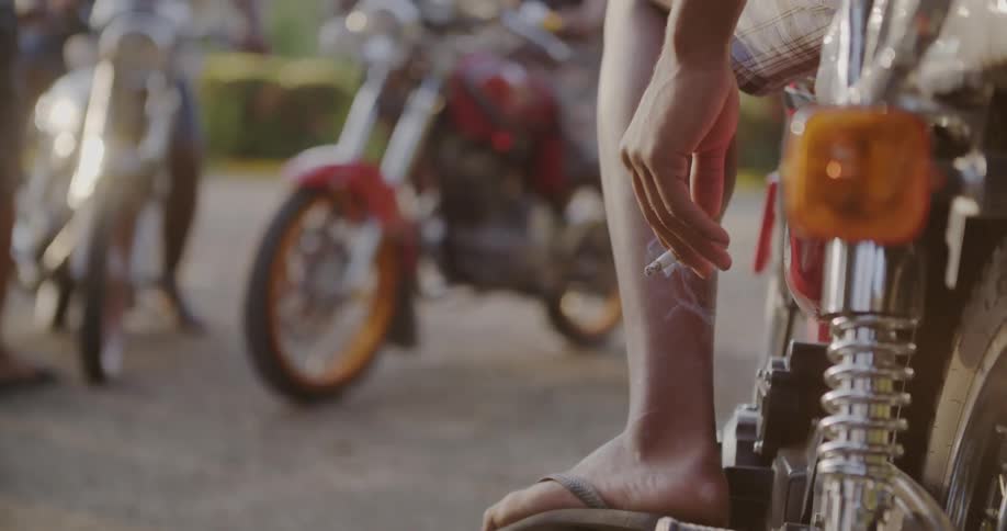 A man sits on a motorcycle and smokes a cigarette