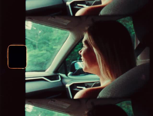 A young woman sits in the passenger seat of a car during a ride talking to the driver at midday