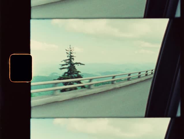 View through a moving car window of an overpass with mountains on the horizon