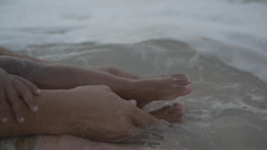 A man rubs someones feet in the beach water
