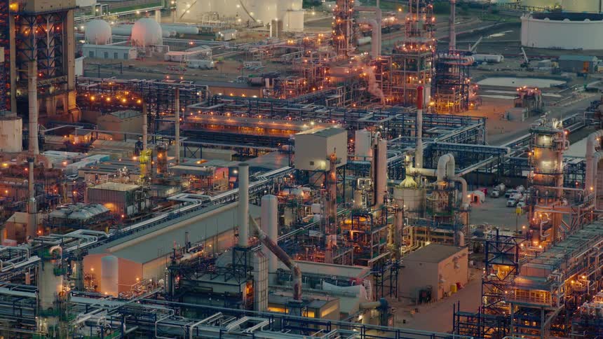 An industrial refinery glows with lights at dusk