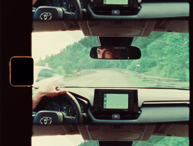 Man driving a car on a treelined road seen through the rearview mirror and dashboard