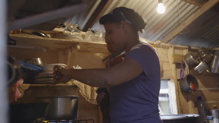 A woman cooks with a child on her hip