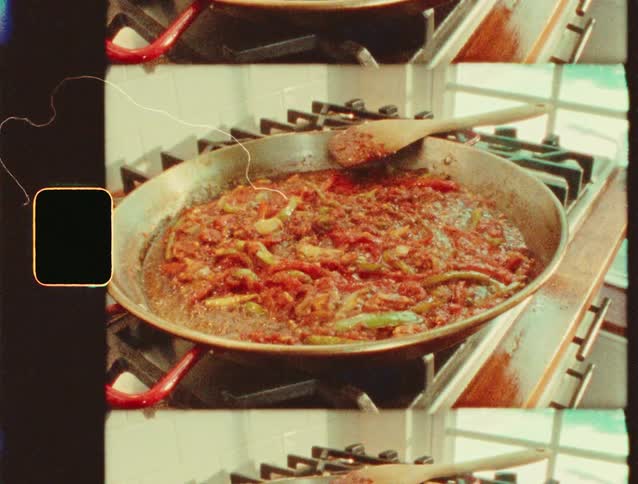 A pan of tomato and pepper sauce simmers on a stovetop with a wooden spoon resting inside
