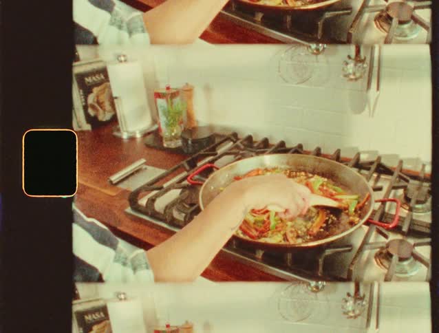 A person in a striped shirt stirs vegetables in a pan on a stovetop captured with a vintage film effect