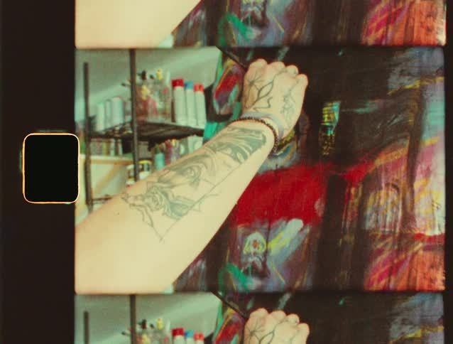 Tattooed arm paints a colorful canvas with a brush in a studio