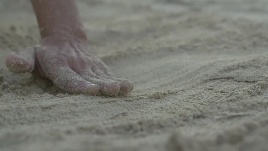Person running their hand across sand