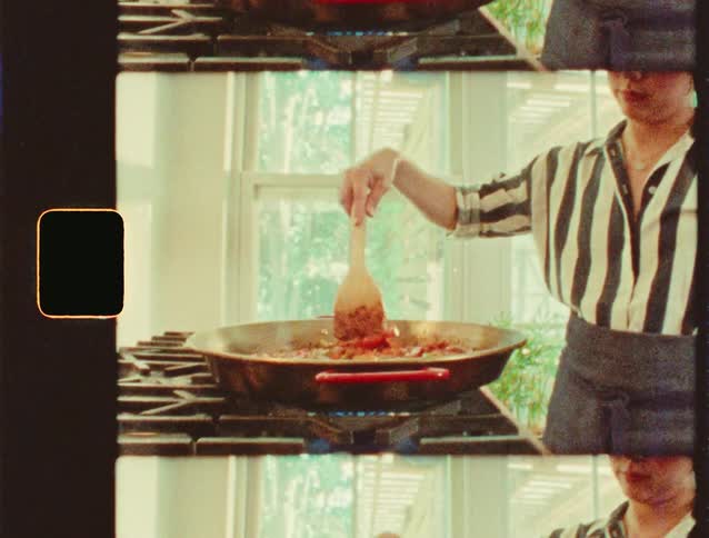 A woman stirs food in a large pan while cooking indoors