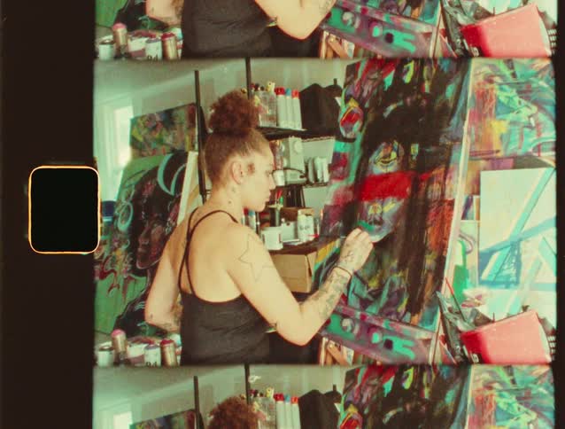 An artist paints a colorful abstract portrait on canvas inside a studio