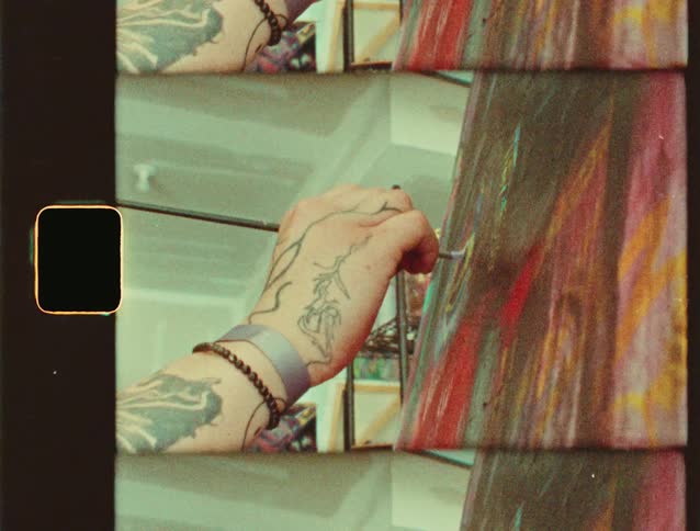 A tattooed hand is painting on a canvas