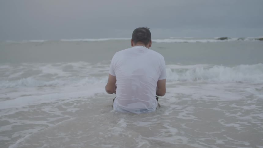 A man sits in the surf at the beach