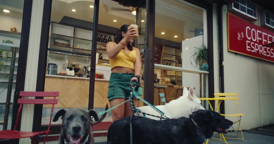 A woman drinks coffee outside while holding dog leashes