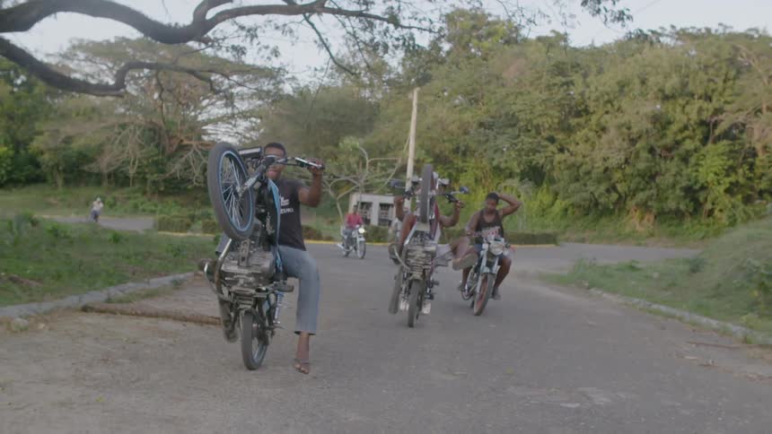 Men riding motorbikes do wheelies on the road