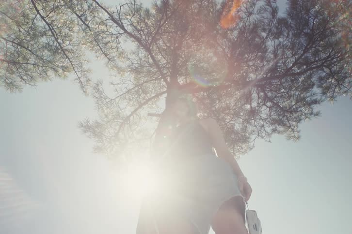 The woman looks up under a tree as the sun shines