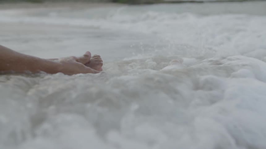 A man sits with a child as ocean waves wash over their legs