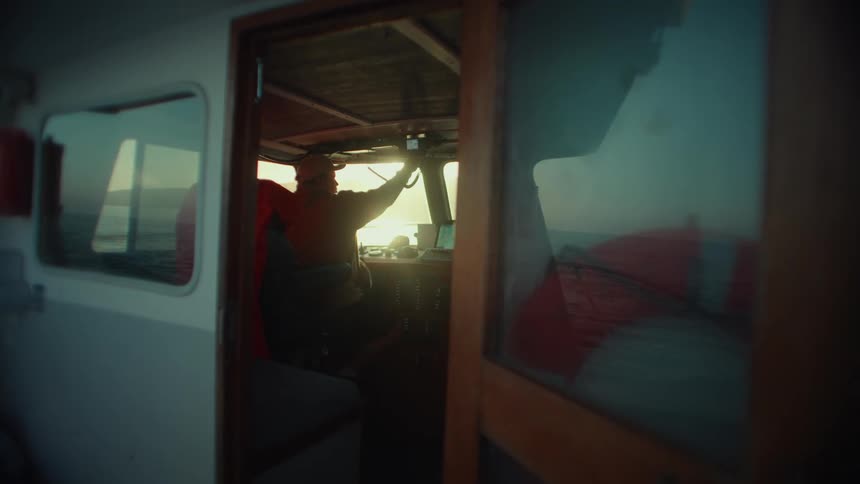Man sitting in the cabin of a boat looks out at the sea while using a radio