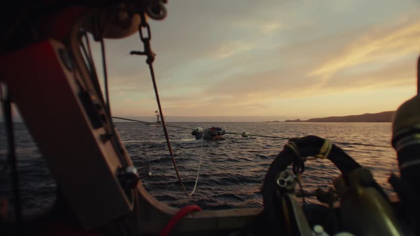 A sunset view from the deck of a boat with another boat anchored in the distance on the open water
