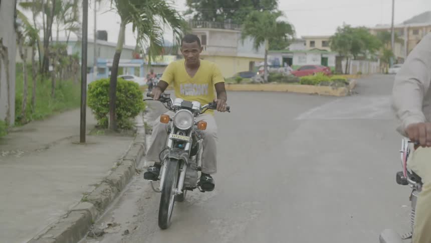 Two men are riding motorcycles in a tropical city