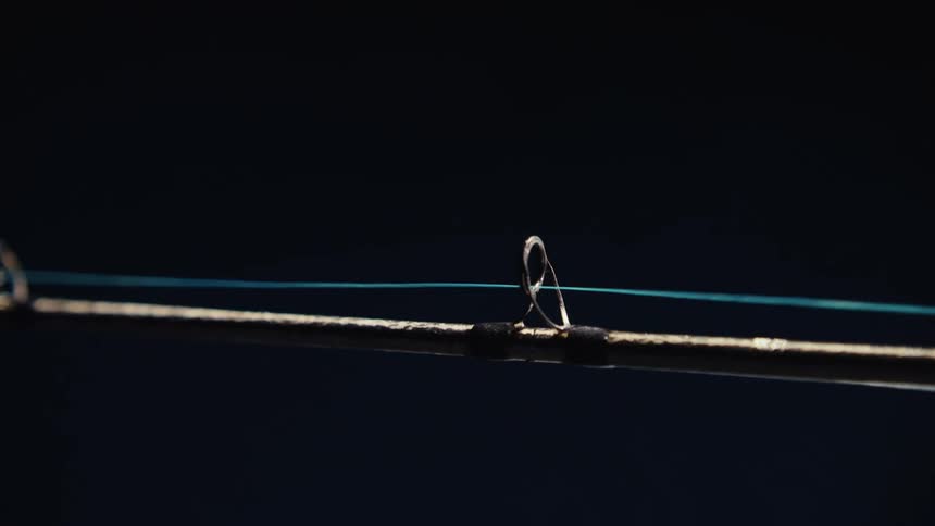 A closeup shows a taut fishing line extending from a rod against a dark background