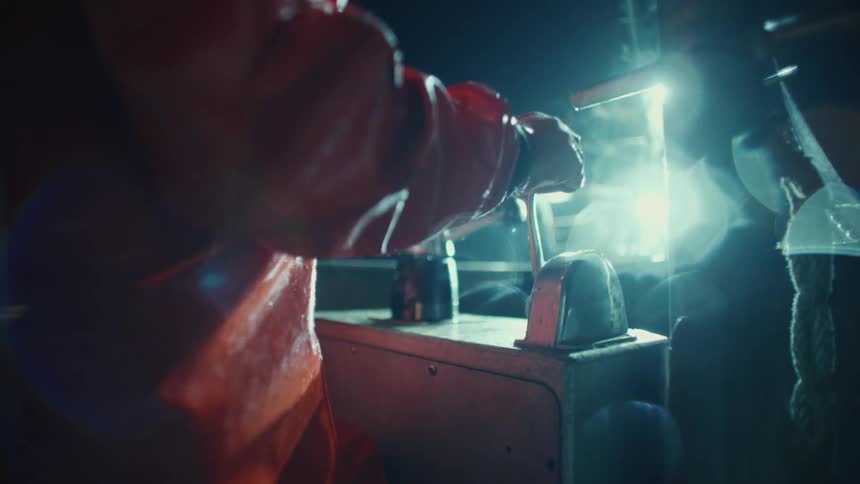 Person in waterproof clothing operates a control lever on a boat lit at night