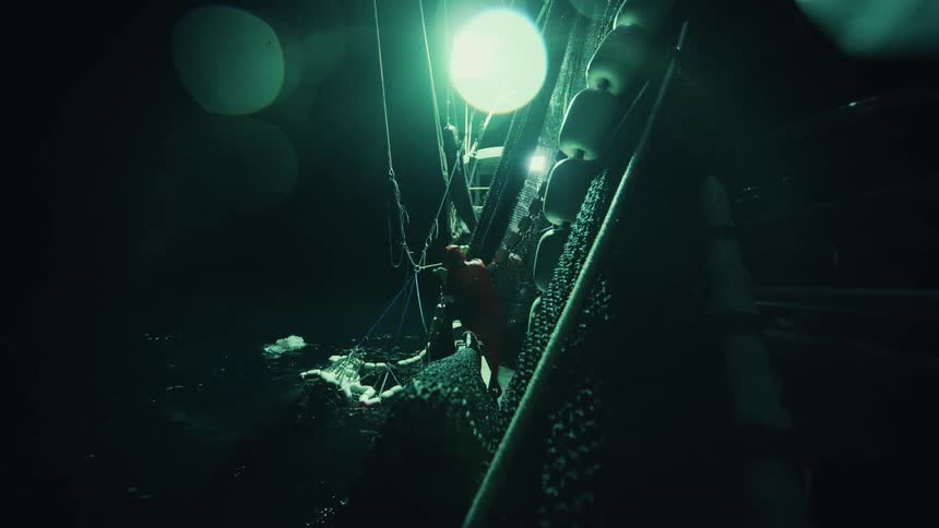 Person wearing red manipulates a net while fishing at night