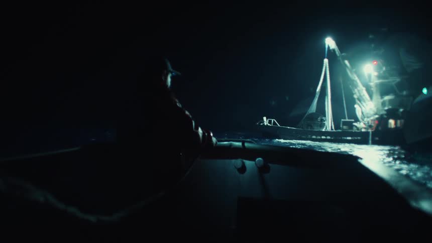 Fisherman in a boat watches illuminated ships at night on the sea
