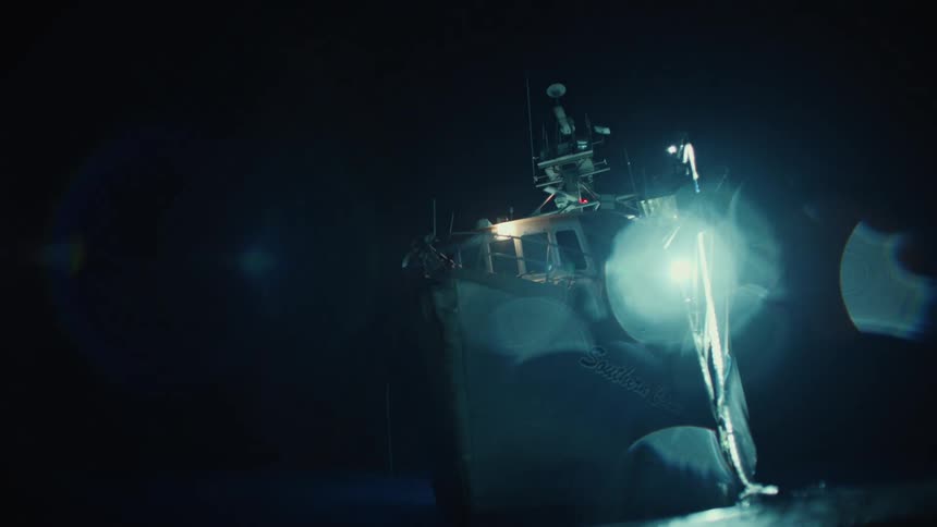 A fishing boat illuminated by powerful deck lights cuts through the darkness of night on open water
