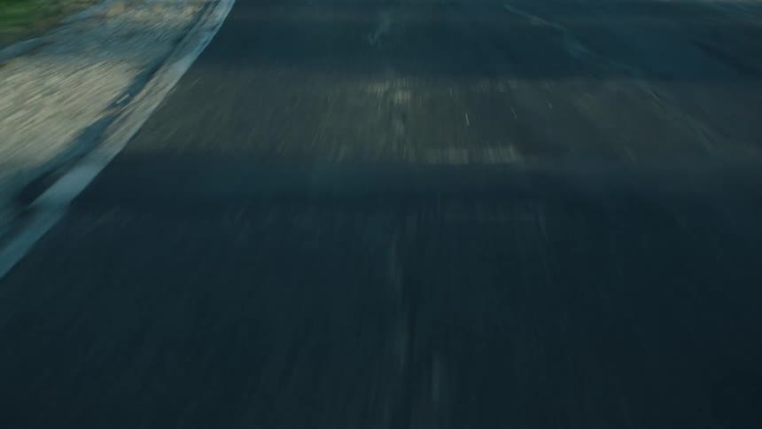 A view of a paved road shows a single yellow center line with shadows cast across the surface