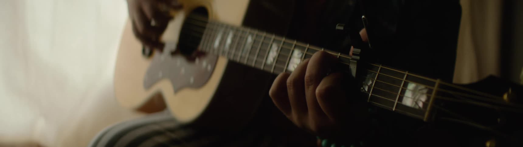Hands play an acoustic guitar with the aid of a capo